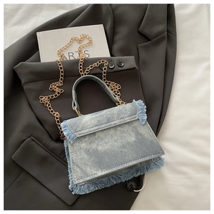 Close-up of denim crossbody bag with fringe edges and gold chain on a black blazer