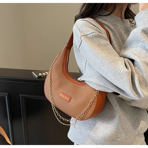 Detail of a brown woven half-moon bag with orange label and gold chain strap decoration