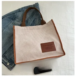 Size comparison of beige corduroy tote bag with brown trim next to a smartphone
