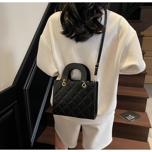 Detail view of black quilted patent leather handbag with gold metal rings and top handle