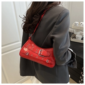 Detail of red faux leather shoulder bag with punk grommets and metal buckles on grey blazer