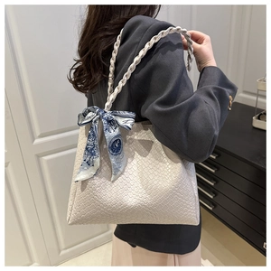 Detail of beige woven tote bag featuring a decorative blue printed silk scarf on handle