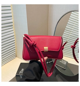 Detail of red leather crossbody bag with gold buckle and unique knotted strap detail