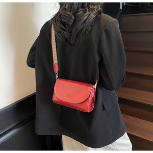 Detail of red leather crossbody bag with wide ethnic-style strap and embossed logo