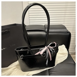 Détail du sac à main en cuir verni noir avec un nœud à carreaux rose et des anneaux en argent