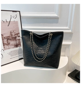 Detail of black tote bag featuring crocodile embossed texture and golden chain strap