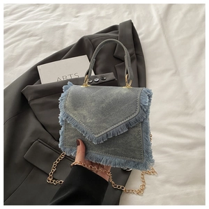 Detailed view of light blue denim mini handbag with fringe trim and golden chain strap