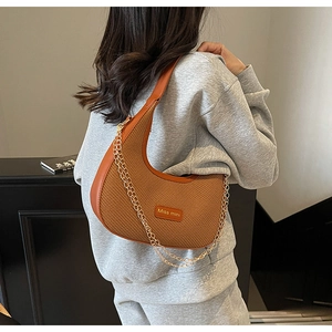 Close-up of brown crescent handbag featuring woven texture and gold chain details