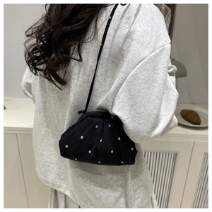 Détail d'un sac bandoulière noir avec broderies florales blanches et texture plissée