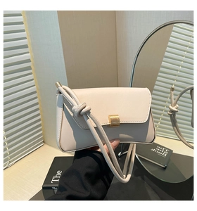 Detail of minimalist cream leather baguette bag with knotted strap and gold metal clasp
