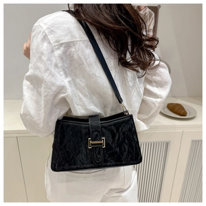 Detail of black pleated baguette bag with gold buckle worn on a shoulder