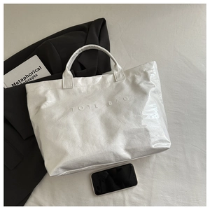 Detail of white tote bag with TOTE BAG embossing and glossy textured surface