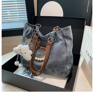 Detail of denim tote bag featuring silver chain, pearl trim, and plush cloud charm