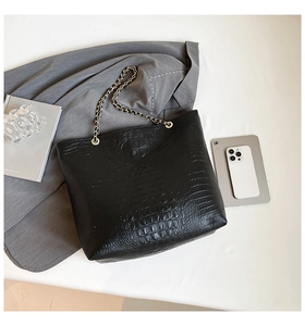 Macro detail of black tote bag with faux crocodile pattern and chain strap