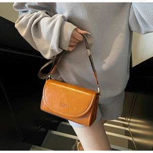 Close-up of orange faux leather crossbody bag with vintage patterned wide strap