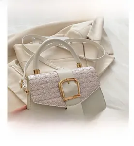 Close-up of beige crossbody bag with woven texture lid and large gold metal buckle