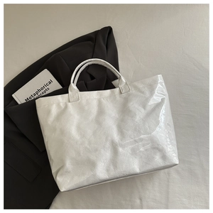 Detail view of white tote bag showing glossy wrinkled texture and reinforced handle