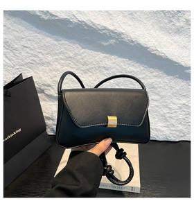 Detail of black leather shoulder bag featuring a gold buckle and knotted strap design
