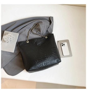 Flat lay of black crocodile pattern tote bag with gold chain strap and modern office props