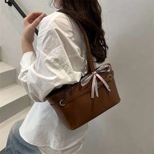 Sac cabas marron avec nœud à carreaux rose porté par une femme en chemise blanche