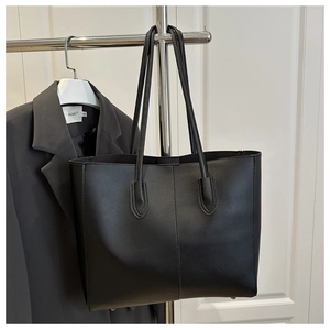 Close-up of black matte faux leather tote bag showing vertical stitching and metal feet