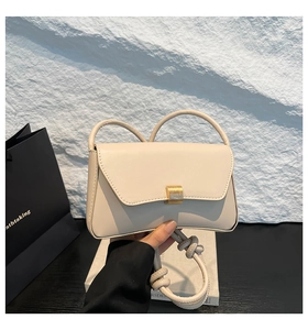 Close-up of cream leather baguette bag with golden metal buckle and knot strap detail