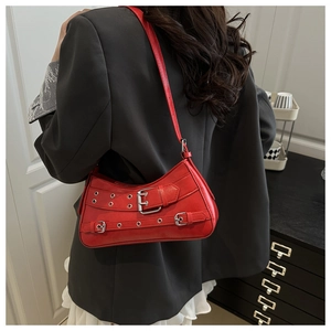 Detail of red punk shoulder bag with silver buckles worn over a grey blazer jacket