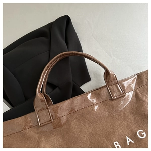Close-up of brown tote bag with glossy crinkle texture and white BAG lettering