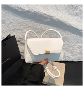 Detail of white leather baguette bag with a gold rectangular metal buckle and ring handle