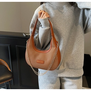 Detail of woven texture and gold chain on brown leather hobo bag held by a model