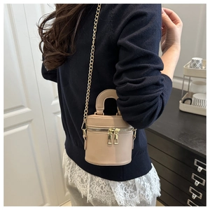 Détail du sac seau beige cylindrique avec double zip doré et bandoulière chaîne