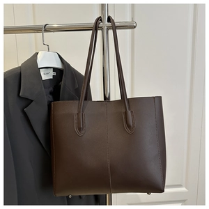 Detail of dark brown leather tote bag with symmetrical stitching and durable metal feet