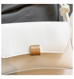 Detail of white baguette bag featuring a textured gold metal buckle and knotted strap