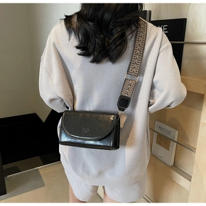 Detailed view of black oil leather crossbody bag with wide geometric pattern strap on model