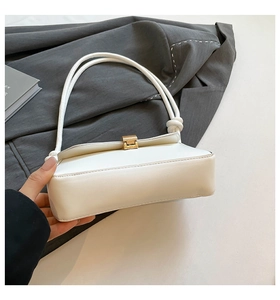 Close-up of creamy white leather baguette bag with gold buckle and knotted strap detail