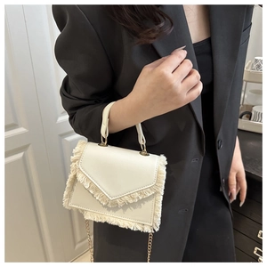 Detail of cream tassel crossbody bag featuring a golden chain strap and leather handle