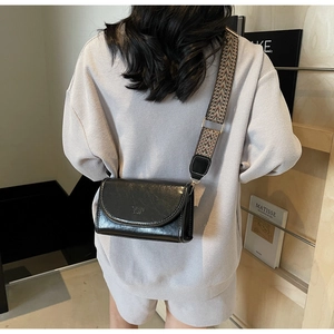 Detail of black glossy small square bag with geometric patterned wide shoulder strap