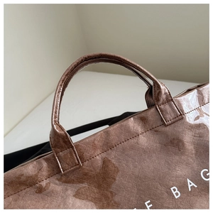 Detailed view of reinforced handle stitching and marbled texture on brown tote bag