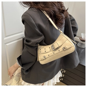 Detailed view of cream leather shoulder bag featuring silver grommets and buckle straps