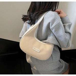 Model wearing a cream woven half-moon shoulder bag with white leather trim and logo