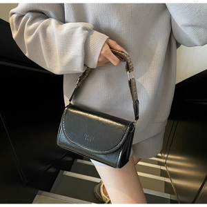 Detail of black crossbody bag with white stitching and patterned woven shoulder strap