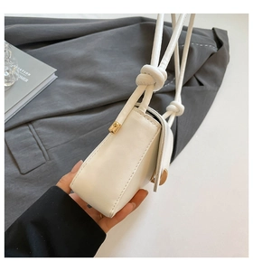 Detail of white PU leather baguette bag with gold buckle and knotted shoulder strap detail