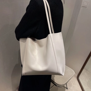 Close-up of a large white minimalist leather tote bag worn over the shoulder