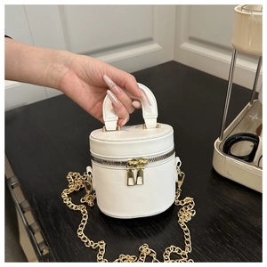 Detail der weißen Mini-Zylindertasche mit goldener Kette auf einer Holzoberfläche