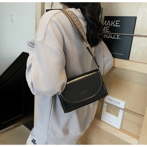 Detail of black glossy leather bag with white stitching and stylish jacquard strap