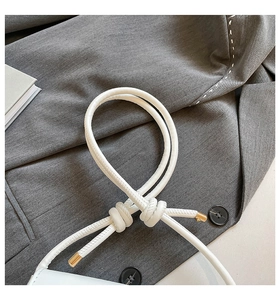 Detail of white leather shoulder bag featuring a unique knotted strap and gold metal tips