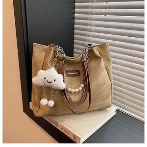 Detail of brown tote bag featuring pearl chain, metal strap, and cloud plush pendant