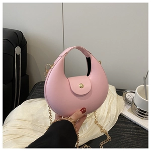 Close-up of pink crescent handbag with gold chain strap on soft white fabric background