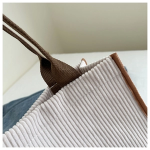 Detailed macro view of wide-stripe corduroy fabric and brown woven handle on a tote bag