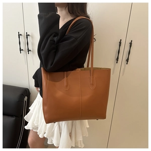 Détail d'un sac cabas en cuir marron montrant des coutures verticales et des clous